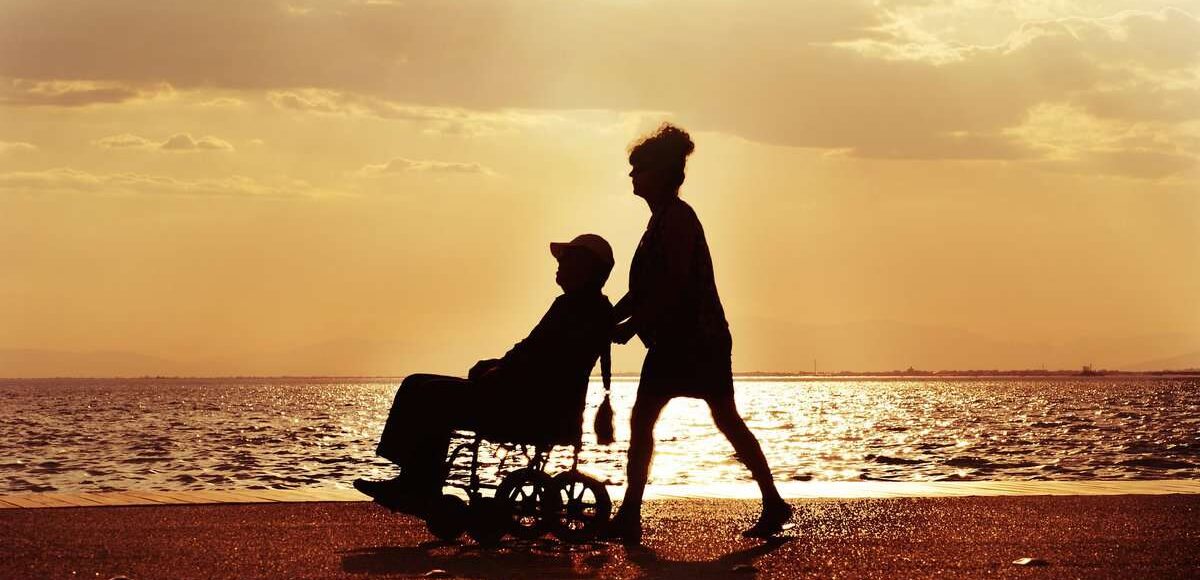 a man pushing a wheel chair next to the ocean.