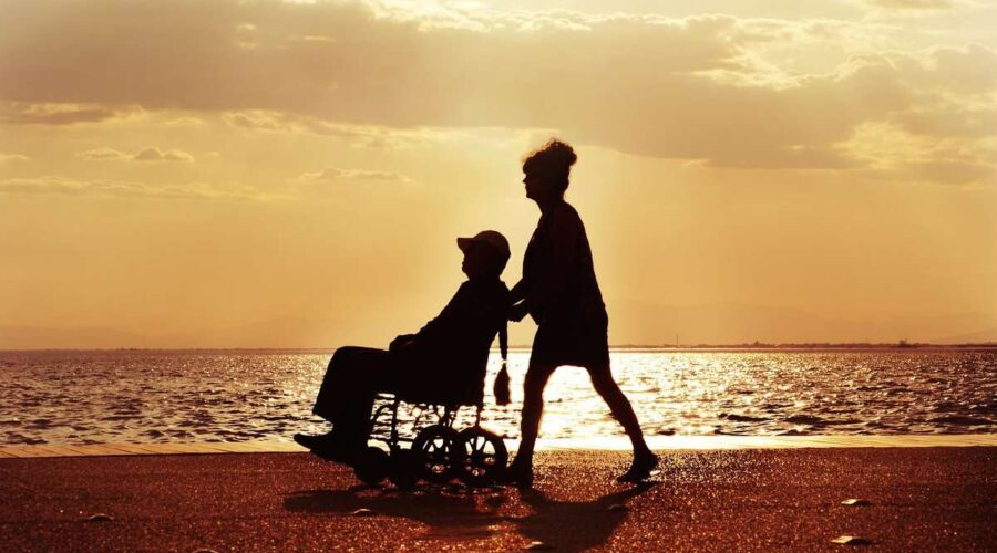 a man pushing a wheel chair next to the ocean.