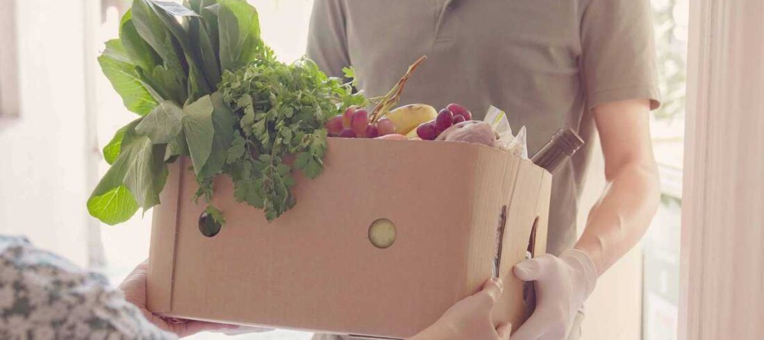 A person distributing food from a box of fruit and vegetables for food support programs.