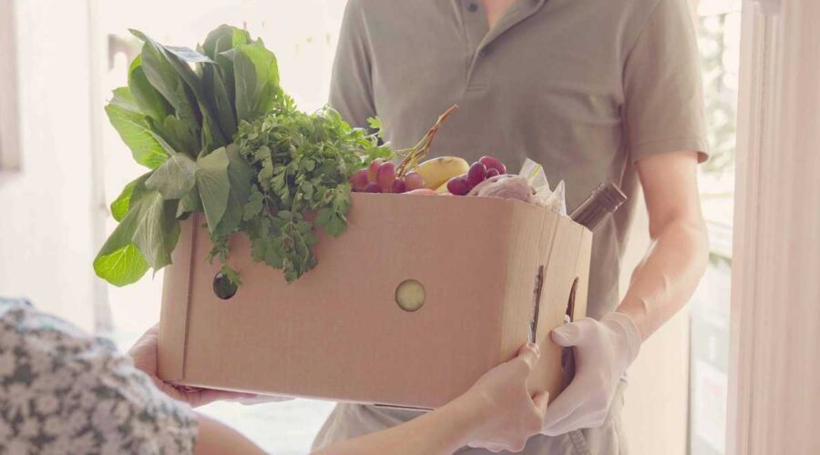 A person distributing food from a box of fruit and vegetables for food support programs.