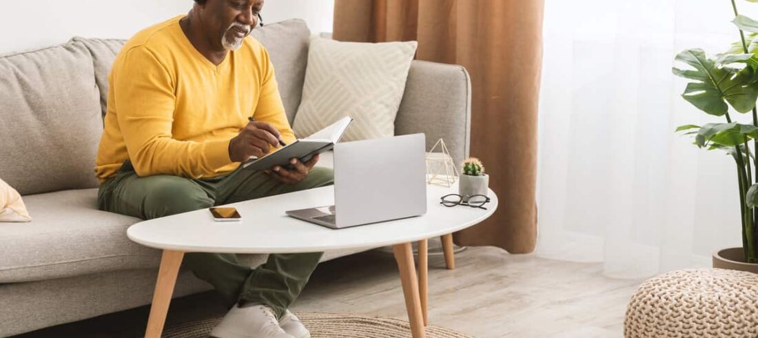 A man on a couch working on a laptop computer to access Benefits.gov.