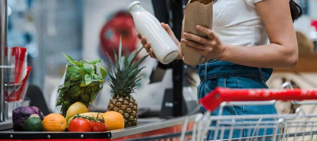 A woman using EBT holding a container of food in a grocery store.
