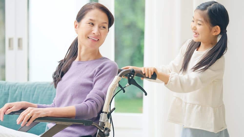 Smiling woman in a wheelchair assisted by a young girl