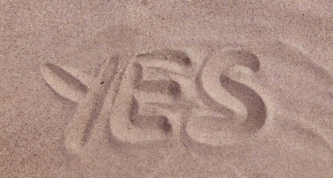 The word yes is written in the sand.