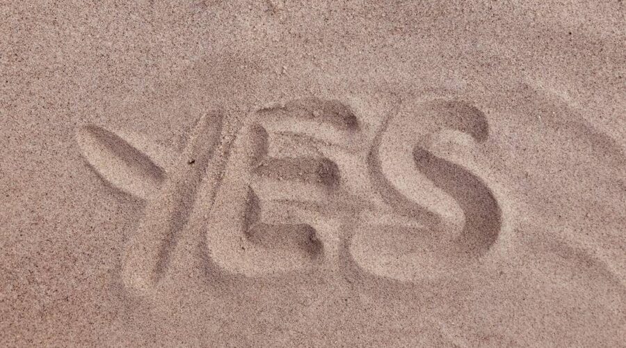 The word yes is written in the sand.